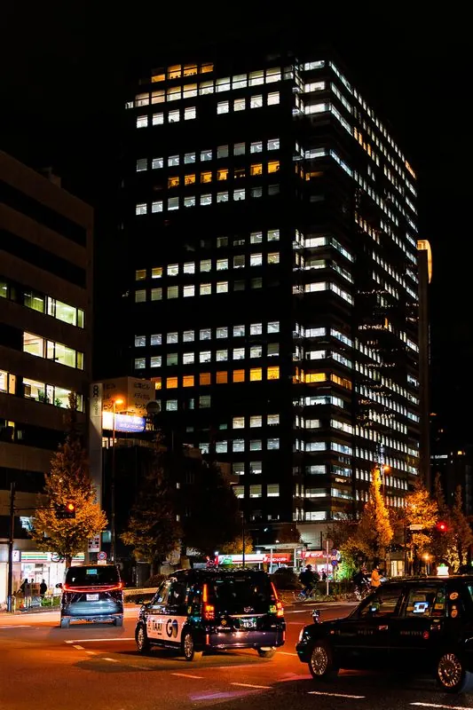 a grid of lit office windows over the taxis waiting at a red light