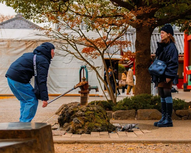 pumping water at the shrine grounds, one leaning on the lever, one waiting her turn