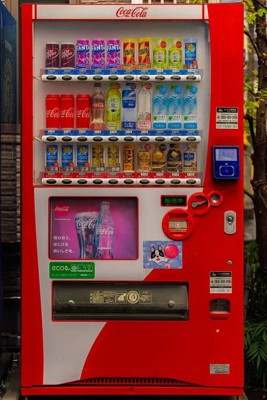 a red coca-cola machine humming on a quiet street, fully stocked and unbothered