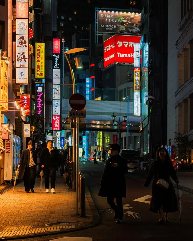 shibuya neon lights the wet sidewalk for people walking home with closed umbrellas